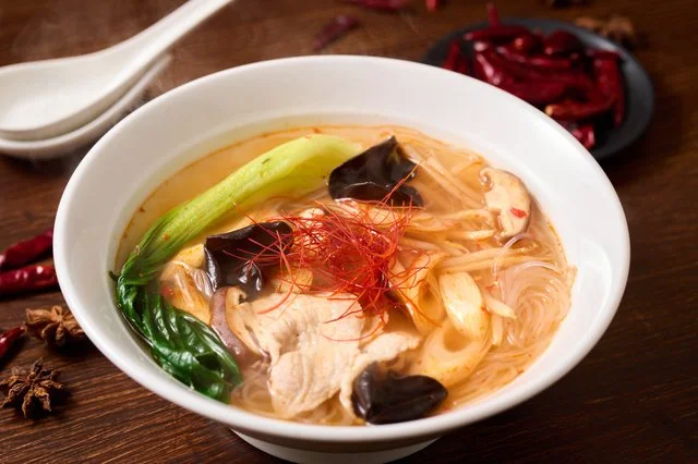 冷蔵ショーケースに青菜、きのこ、練り物、麺が整然と並び、手前でボウルに具材を選ぶ様子